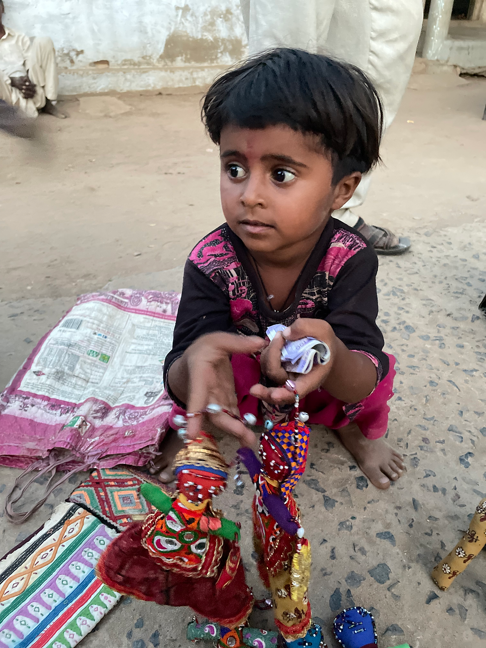 A young child from the Vadha community showcases handcrafted dolls made by the women of the community, an effort to support their livelihood - Photo @ Siân Warren