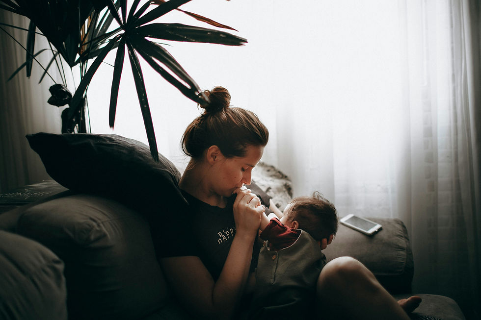 A woman sits on a sofa holding a baby and kissing the baby's hand