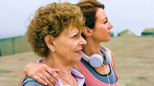 Young woman with arm around the shoulder of older woman, from the chest up looking out to and facing the right.