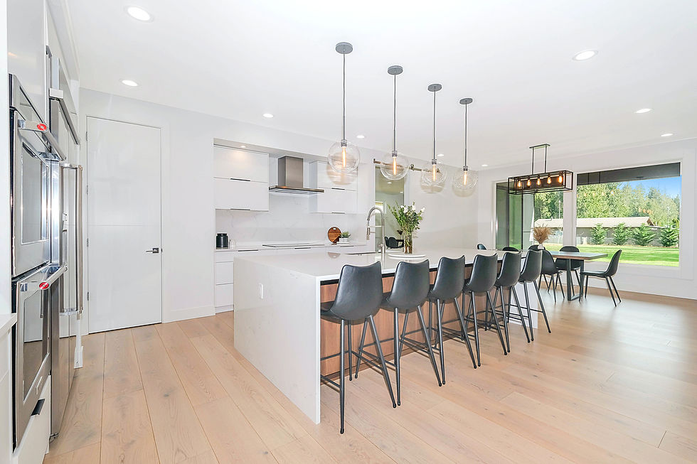 A bright modern kitchen with a white island, black stools and glass pendant lights.