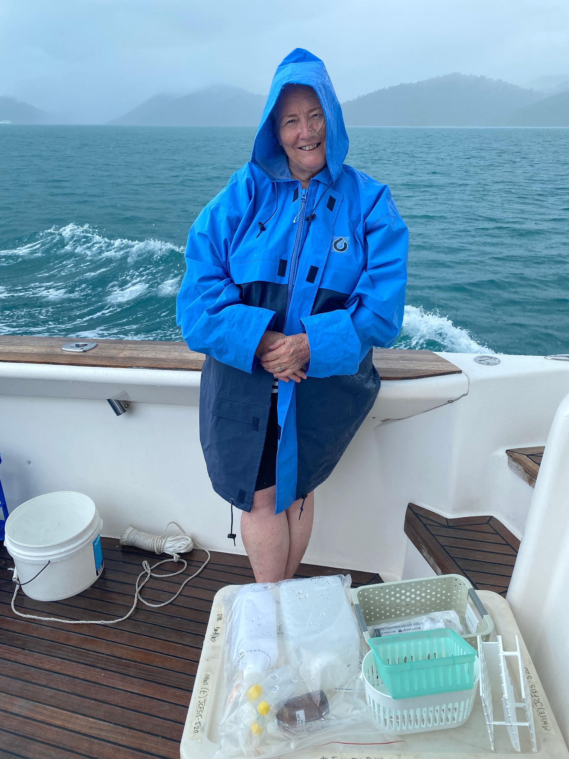 A person in a raincoat standing on a moving boat, smiling at the camera