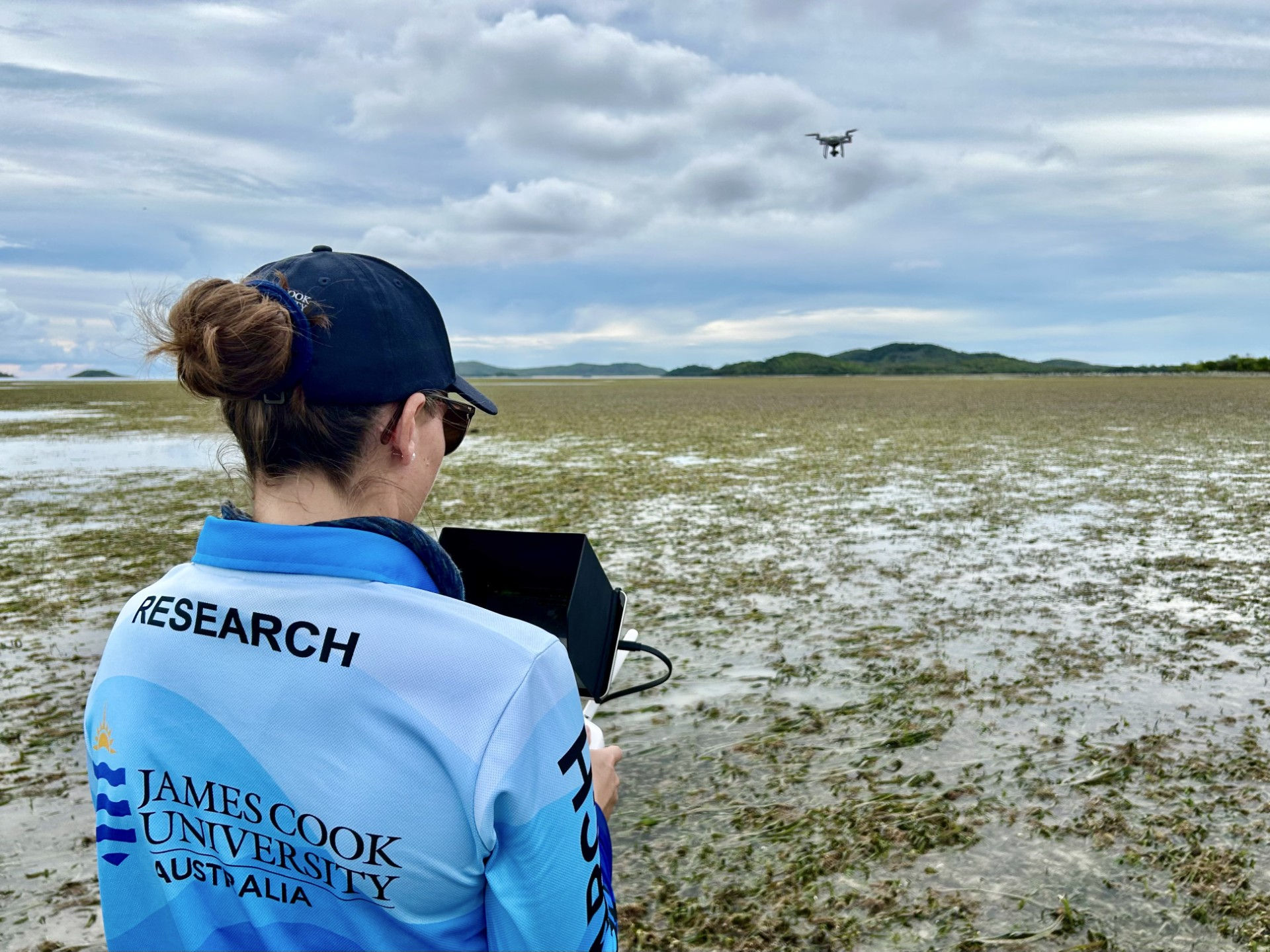 A person flying a drone over a seagrass meadow at low tide