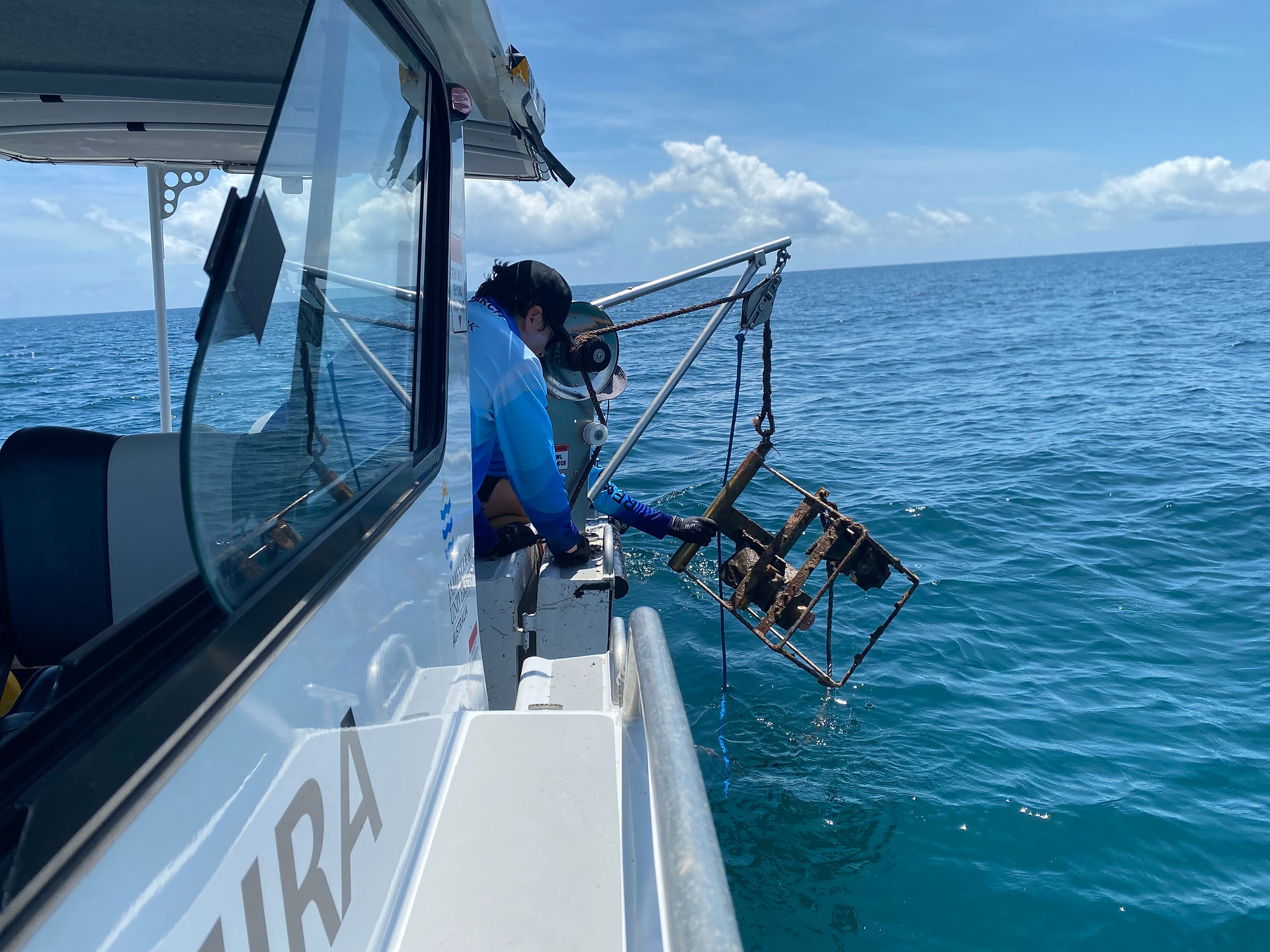 Two people pulling up a camera in a metal frame onto a boat
