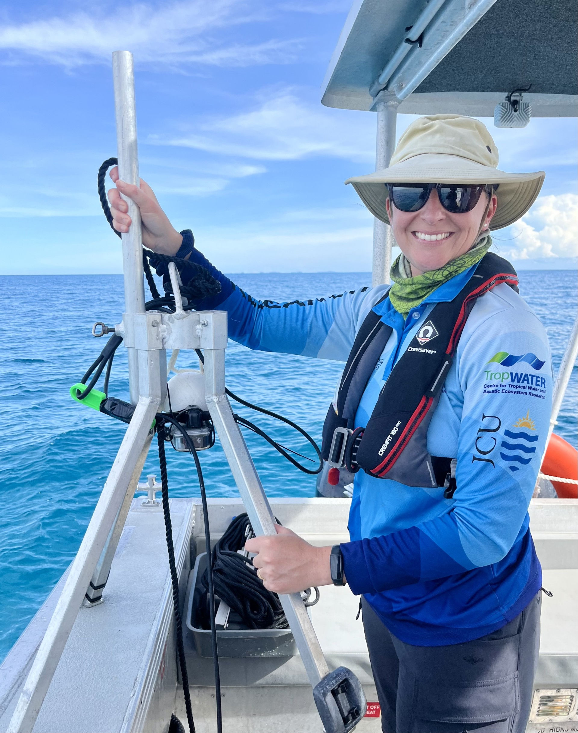 A person on a boat, holding a drop camera frame and smiling at the camera