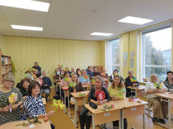 Pedagogi sēž klasē ar papīra ziediem