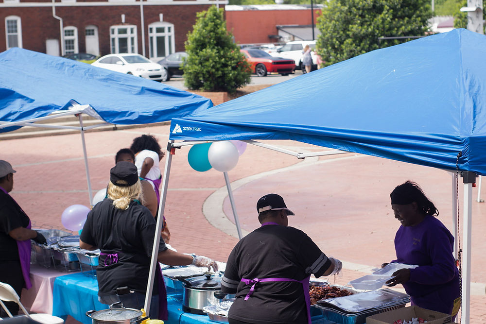 People serving food at an outdoor event under blue tents