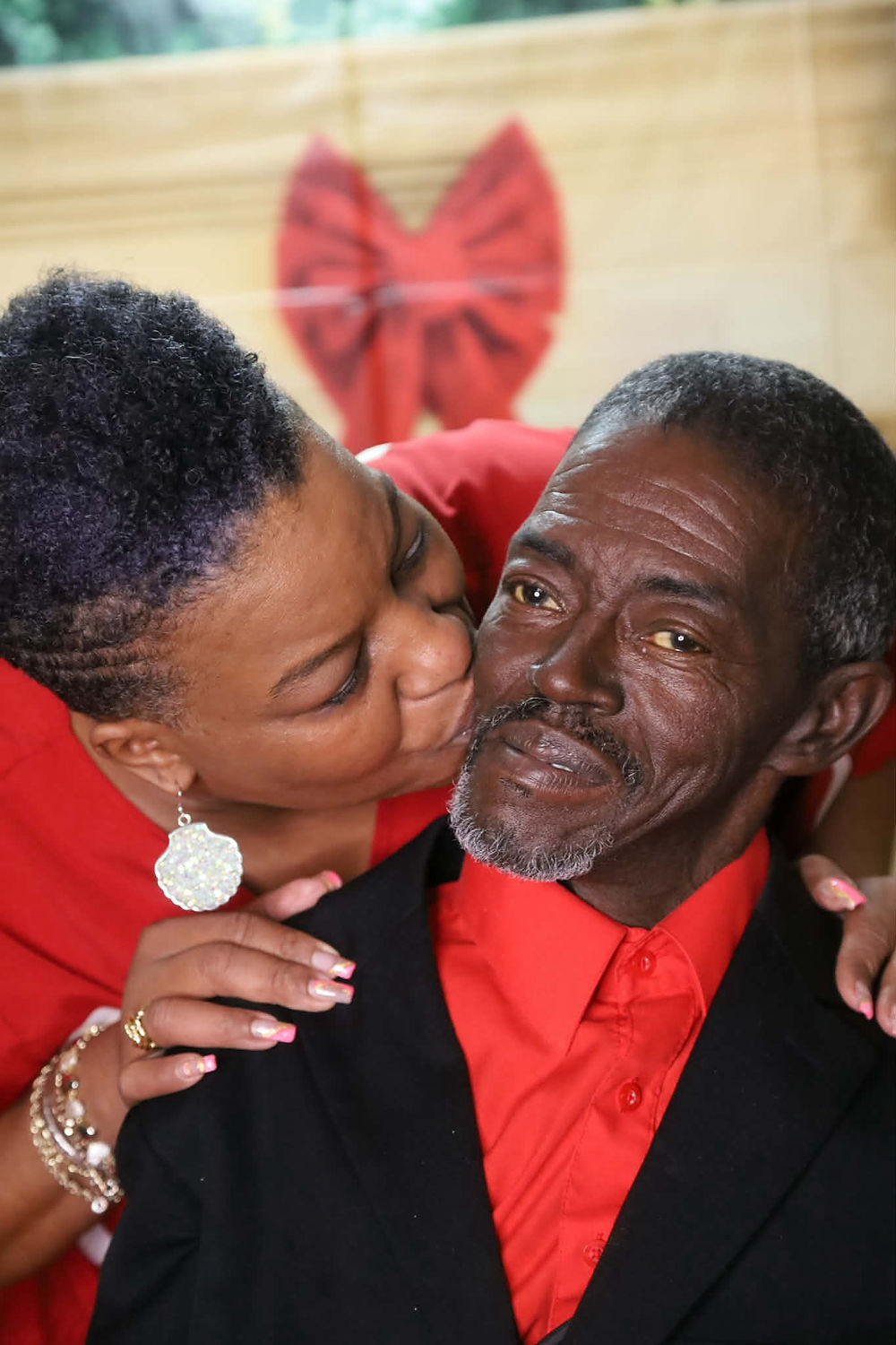 Woman kissing older man on cheek, both wearing red