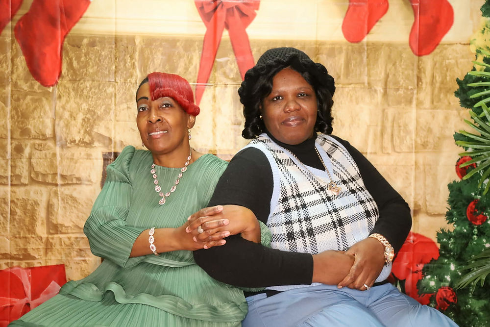 Two women hold hands in front of a Christmas background.