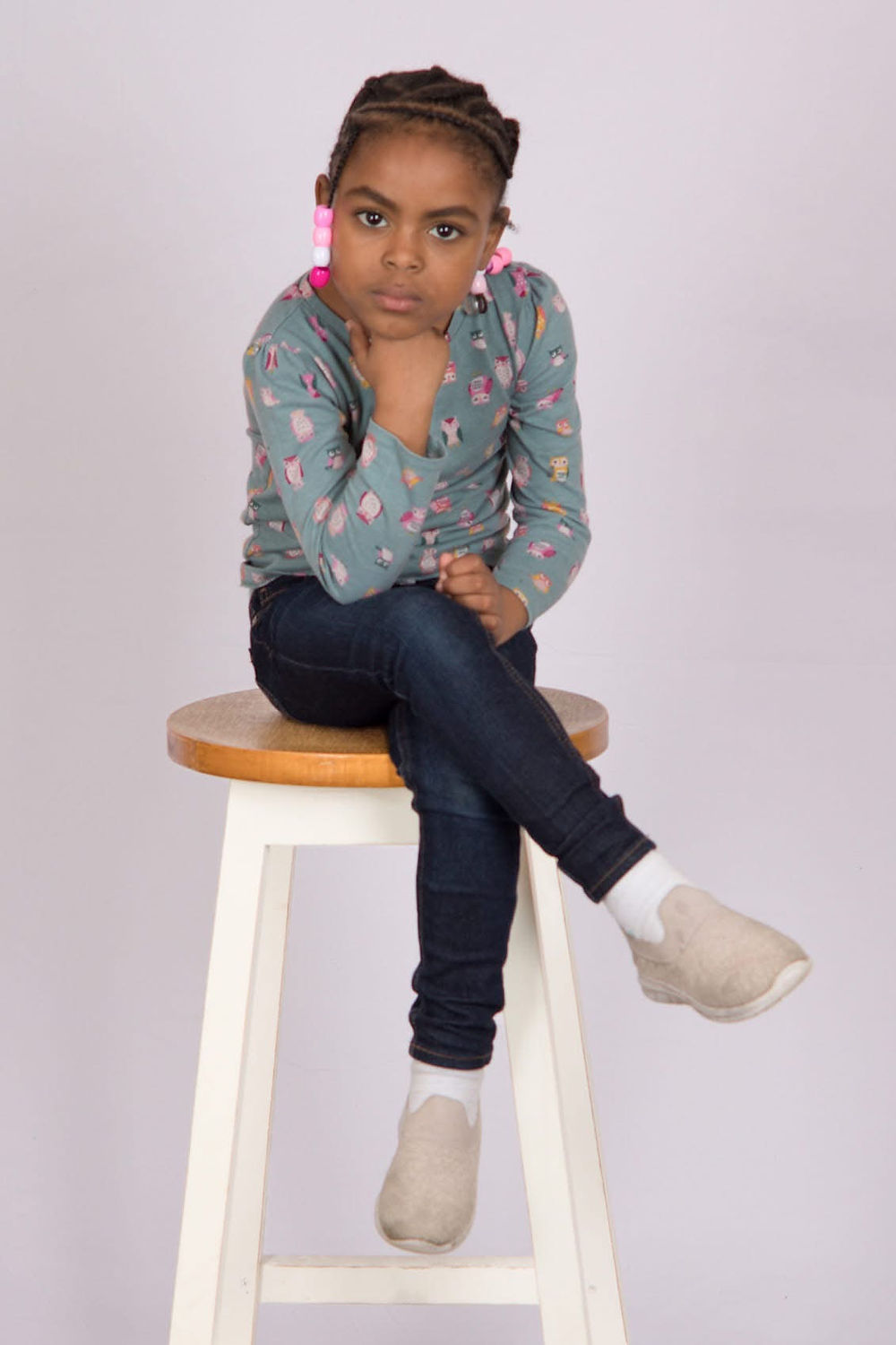 Young girl with braids and serious expression on stool