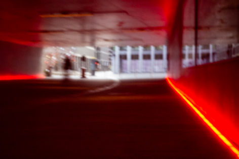 Tunnel éclairé en rouge, silhouettes humaines et véhicules. JRP photographe.