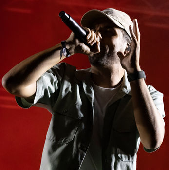 Un rappeur sur scène, micro en main, lumière rouge. Concert live ambiance. JRP photographe