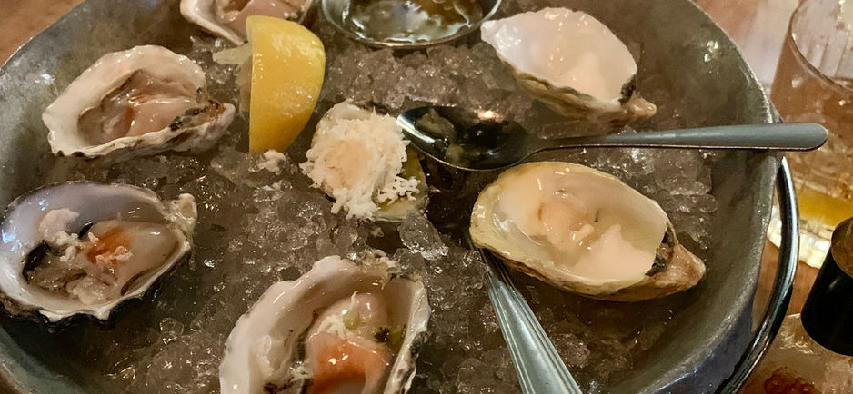 A plate of oysters on the half shell with lemon and horse radish garnish served on an iced platter