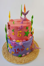 Mermaid birthday cake decorated with ocean-coloured buttercream, edible seashells, and a fondant mermaid topper.