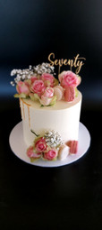 Seventieth birthday cake decorated with fresh flowers, macarons, and a custom topper.