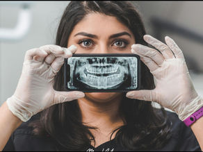 Woman wearing gloves holds a phone with a dental X-ray covering her mouth. Background is blurred, mood is professional and curious.
