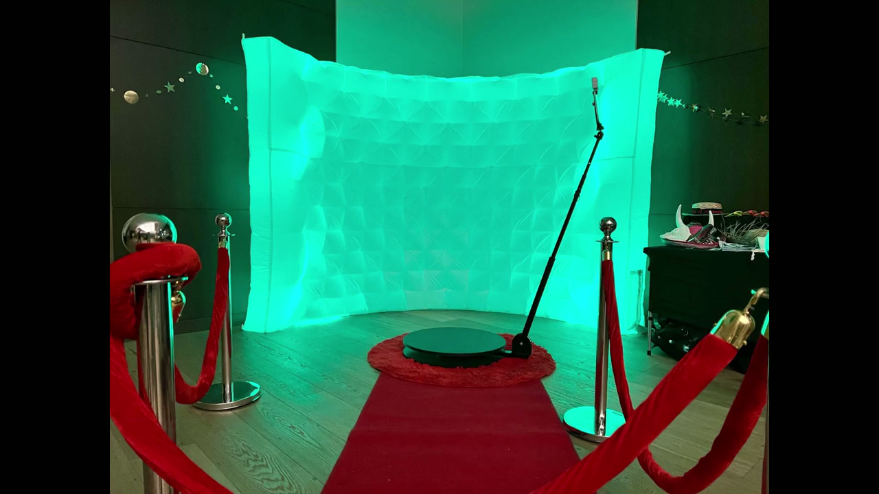 Inflatable LED photo booth glowing green beside a 360 spin booth with red carpet and velvet ropes