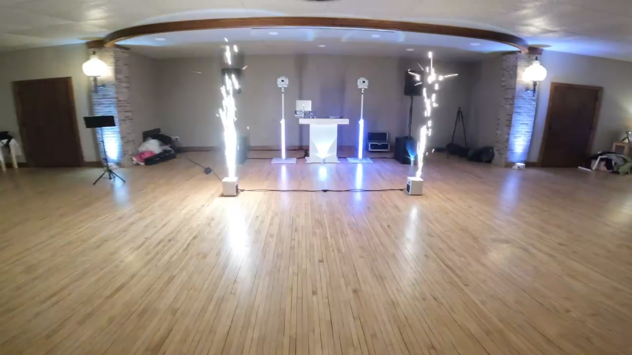 Cold sparklers firing beside the all-white booth and white speaker towers in an empty hall