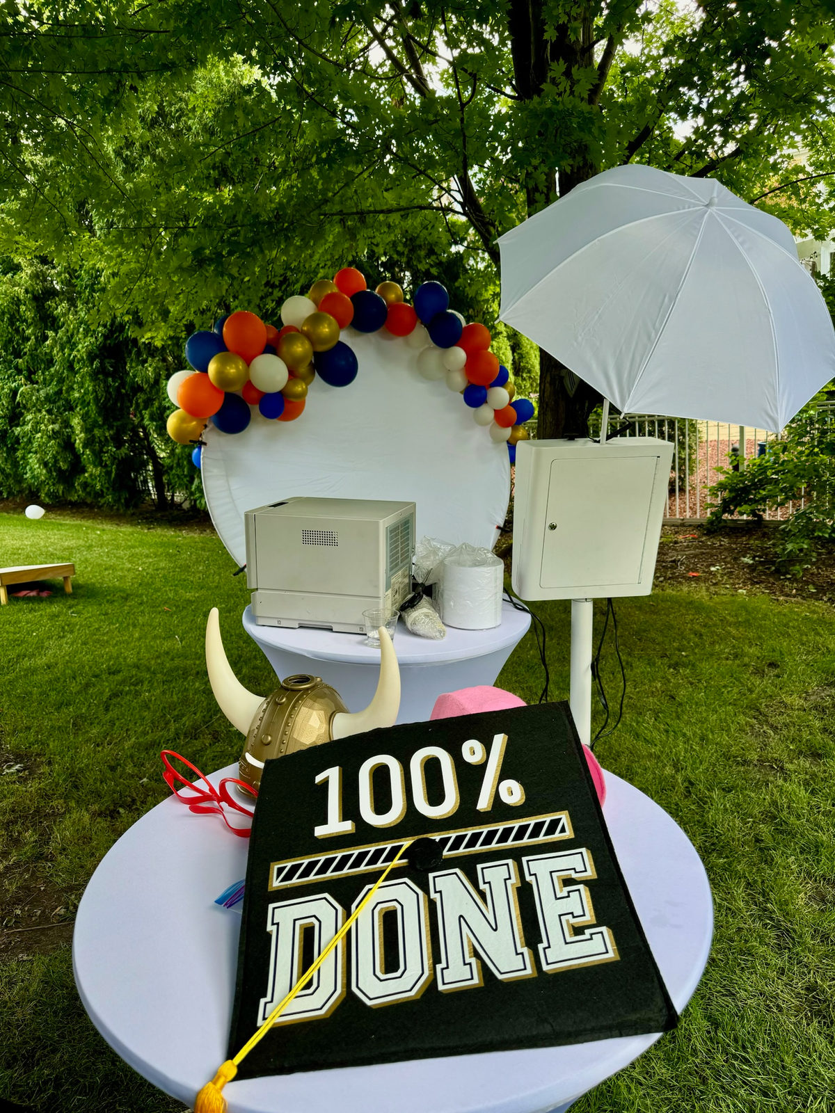 Backyard graduation photo booth with an orange, navy and gold balloon garland and props