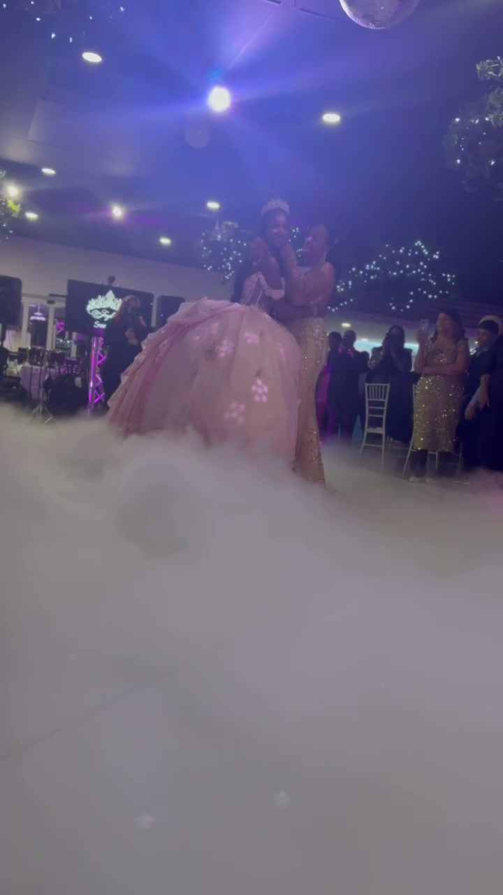 Quinceañera in a pink gown dancing on a cloud of low fog under blue lights