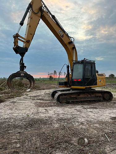 Escavadeira Caterpillar amarela manuseando galhos sob um céu nublado, trabalho em campo.