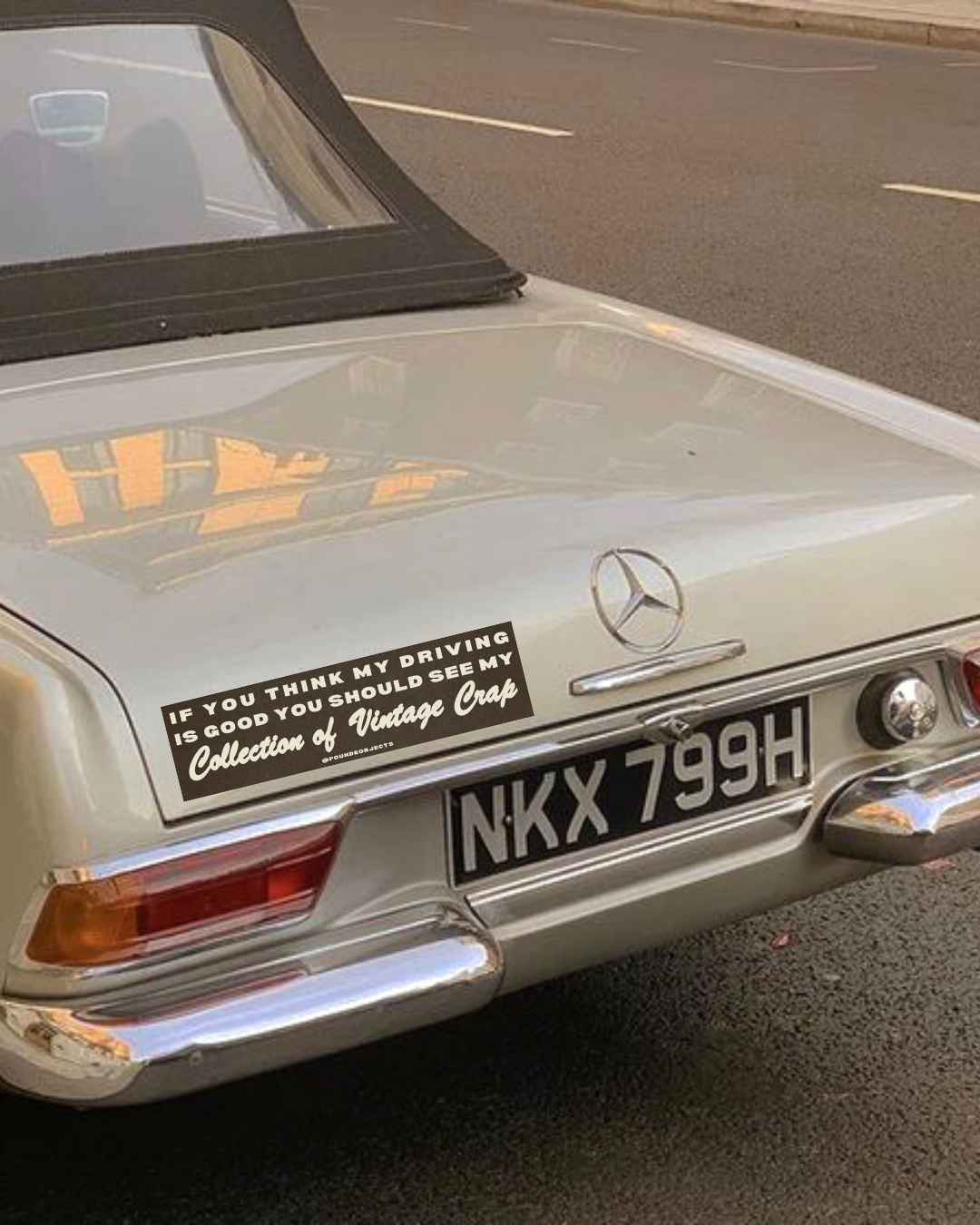 A classic car with a bumper sticker saying "if you think my driving is good, you should see my collection of vintage crap"