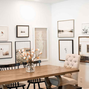 a view of a art gallery wall behind a dining room table with a vase of flowers on it
