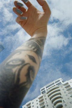 Tattoos on arm reaching toward blue sky, building below