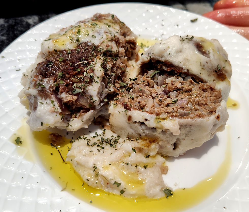 Two stuffed cabbage rolls on a white plate, topped with herbs and drizzled with olive oil. The rolls are cut open, revealing filling.