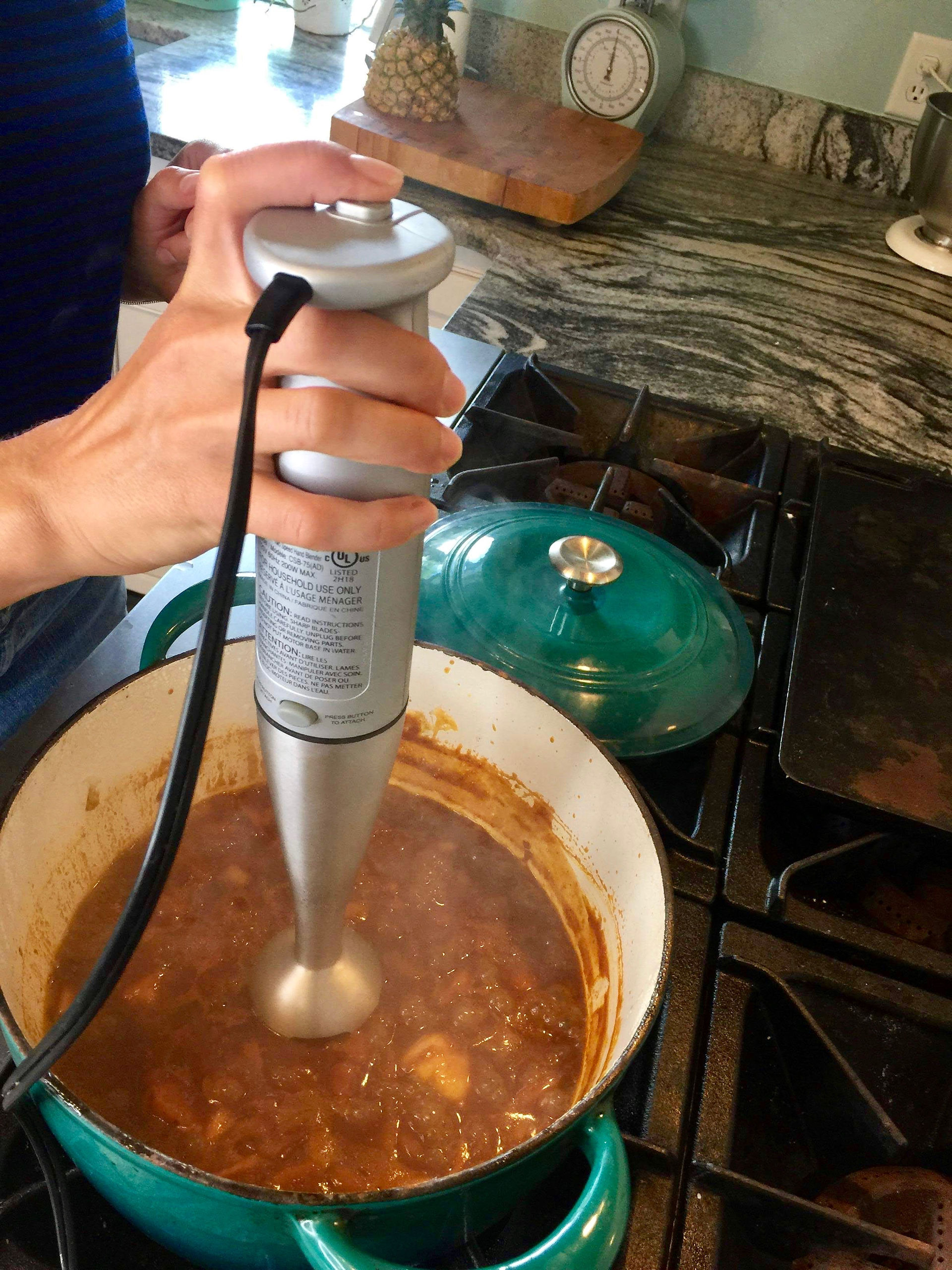 Using an immersion blender to blend together all ingredients for pineapple barbecue sauce