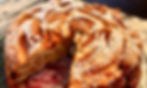 Apple cake with powdered sugar on top, a slice missing. Served on a clear glass plate on a marble countertop. Warm, cozy feel.