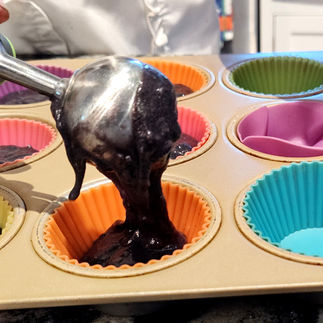 cookie scoop pouring black batter into silicon cupcake cups