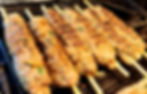 Grilled kebabs on skewers sizzling on a grill pan, with a golden-brown crust and specks of herbs, creating a savory and appetizing scene.