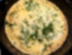 Golden omelet or crepe in a black skillet, topped with fresh dill and melted butter, warm and rustic cooking scene
