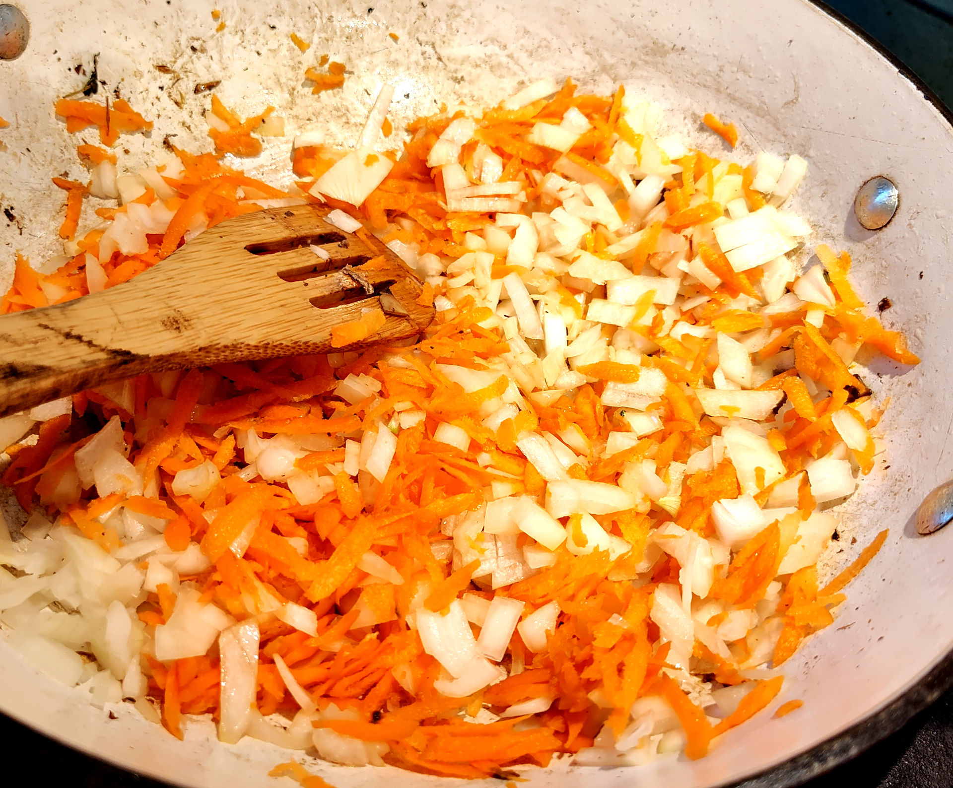 carrots, onion and garlic on a pan cooking, wooden scoop