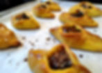 Golden pastries with dark filling on a baking sheet, lightly glazed, on parchment paper with oil spots. Warm, fresh-baked appearance.