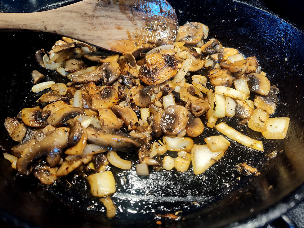Sautéed mushrooms and onions sizzling in a black skillet, stirred with a wooden spoon, warm golden-brown close-up.