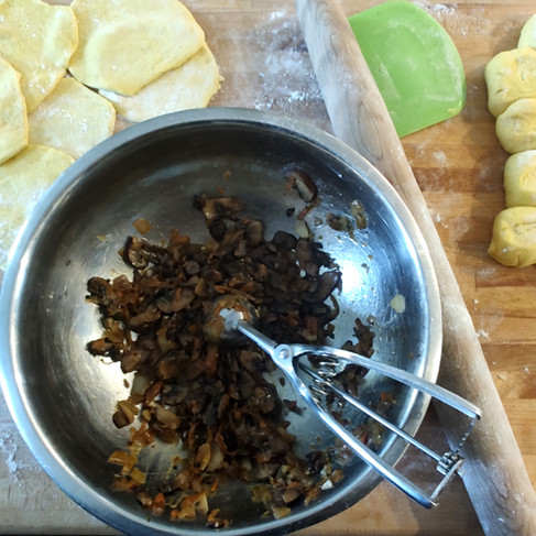 mushroom filling in a bowl, scoop, pieces of dough on a wooden board and circles of the dough 