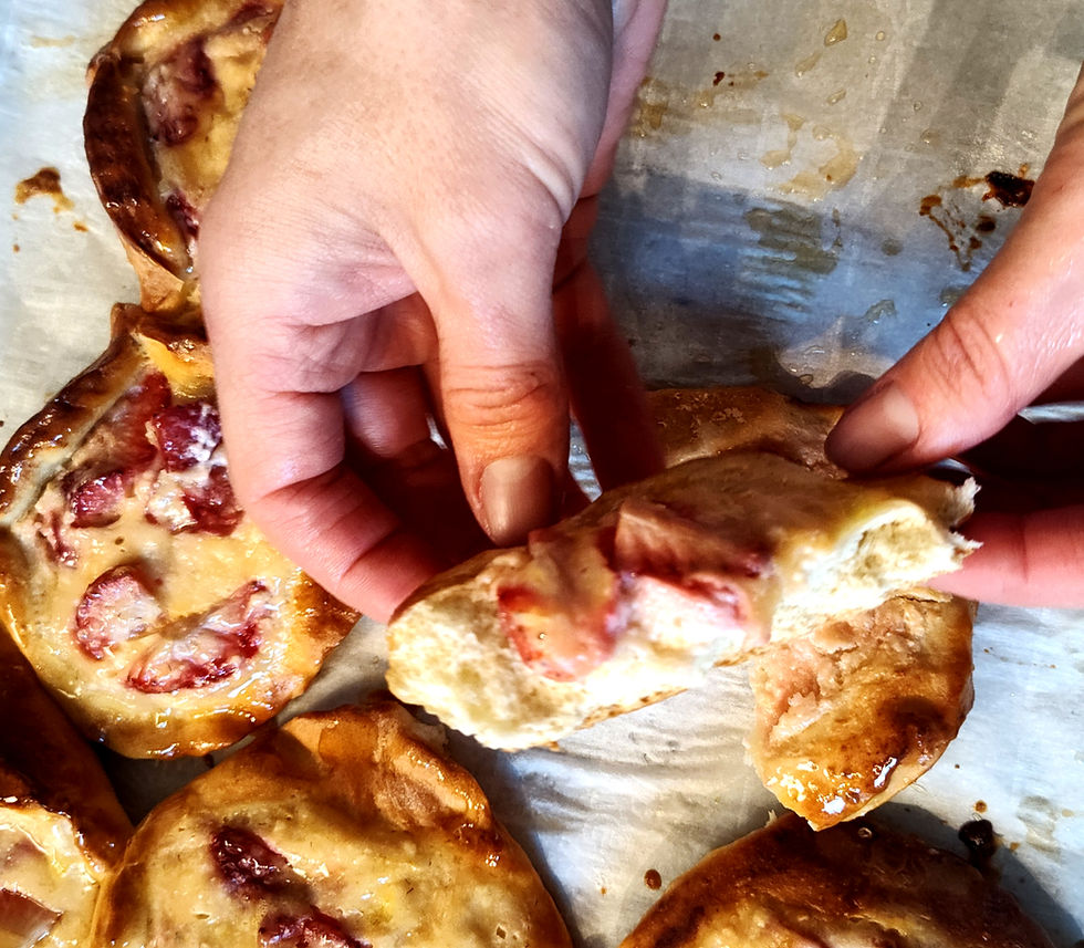 Hands holding freshly baked pastries with visible strawberries, set on parchment paper. The pastries are glossy and golden brown.
