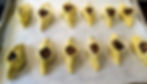 Unbaked yellow dumplings filled with dark veggies on parchment-lined baking tray, neatly arranged in rows.