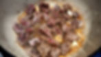 Beef chunks and garlic cloves sizzle in a pan, surrounded by rich, brown juices, showcasing a hearty cooking scene.