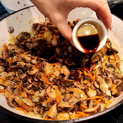 adding soy sauce to the pan with a sauté mixture of veggies and mushrooms