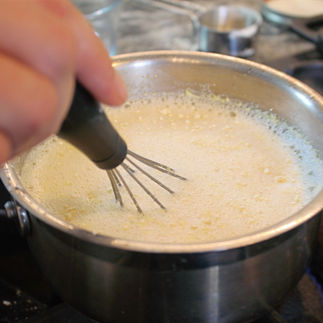 with hand whisk stirring white liquid 