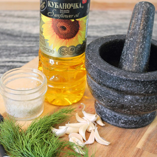 on a wooden cutting board bottle of oil, salt, brush, garlic, dill, mortar and pestle 