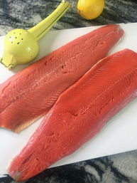 Two salmon fillets on a cutting board next to a lemon juicer