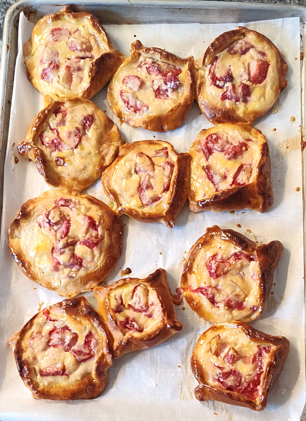Freshly baked pastries with golden, flaky crusts and strawberry filling on a parchment-lined baking tray. Warm and inviting.