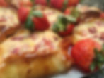 Close-up of glazed pastries topped with fresh strawberries on a plate. The pastries are golden and glossy, creating an appetizing scene.