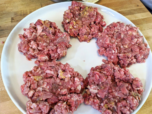Five uncooked hamburger patties on a white plate