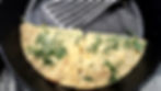 Folded dill omelet in a black skillet with a metal spatula, close-up of a simple homemade breakfast.