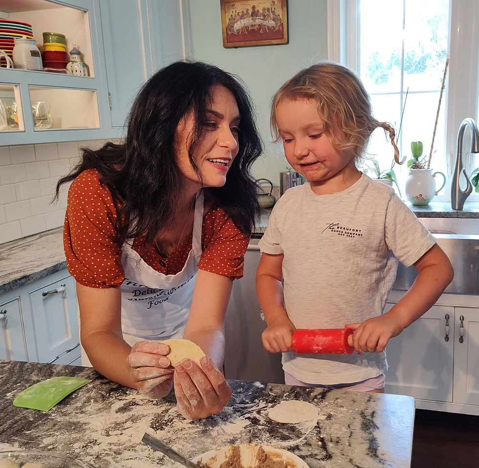 Woman and child baking in a cozy kitchen. Woman holds dough while child uses a red rolling pin. Light blue cabinets, bright window.