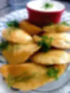 Golden-brown pierogi on a plate garnished with dill and green onions. Accompanied by a red ramekin of sour cream. Light, inviting mood.
